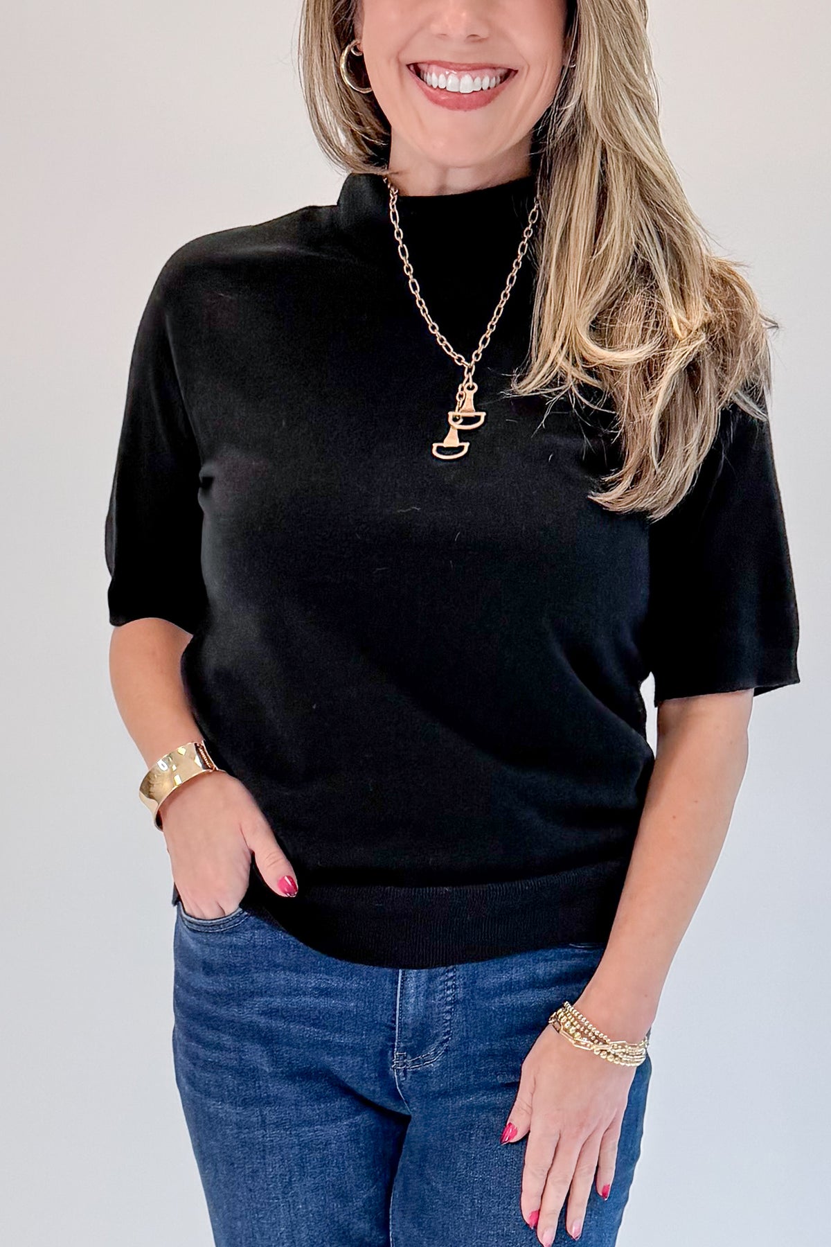 Front detail view of woman wearing Swagger Boutique’s Black Short Sleeve Turtleneck Sweater with jeans against white studio background.