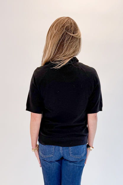 Back view of woman wearing Swagger Boutique’s Black Short Sleeve Turtleneck Sweater with jeans against white studio background.