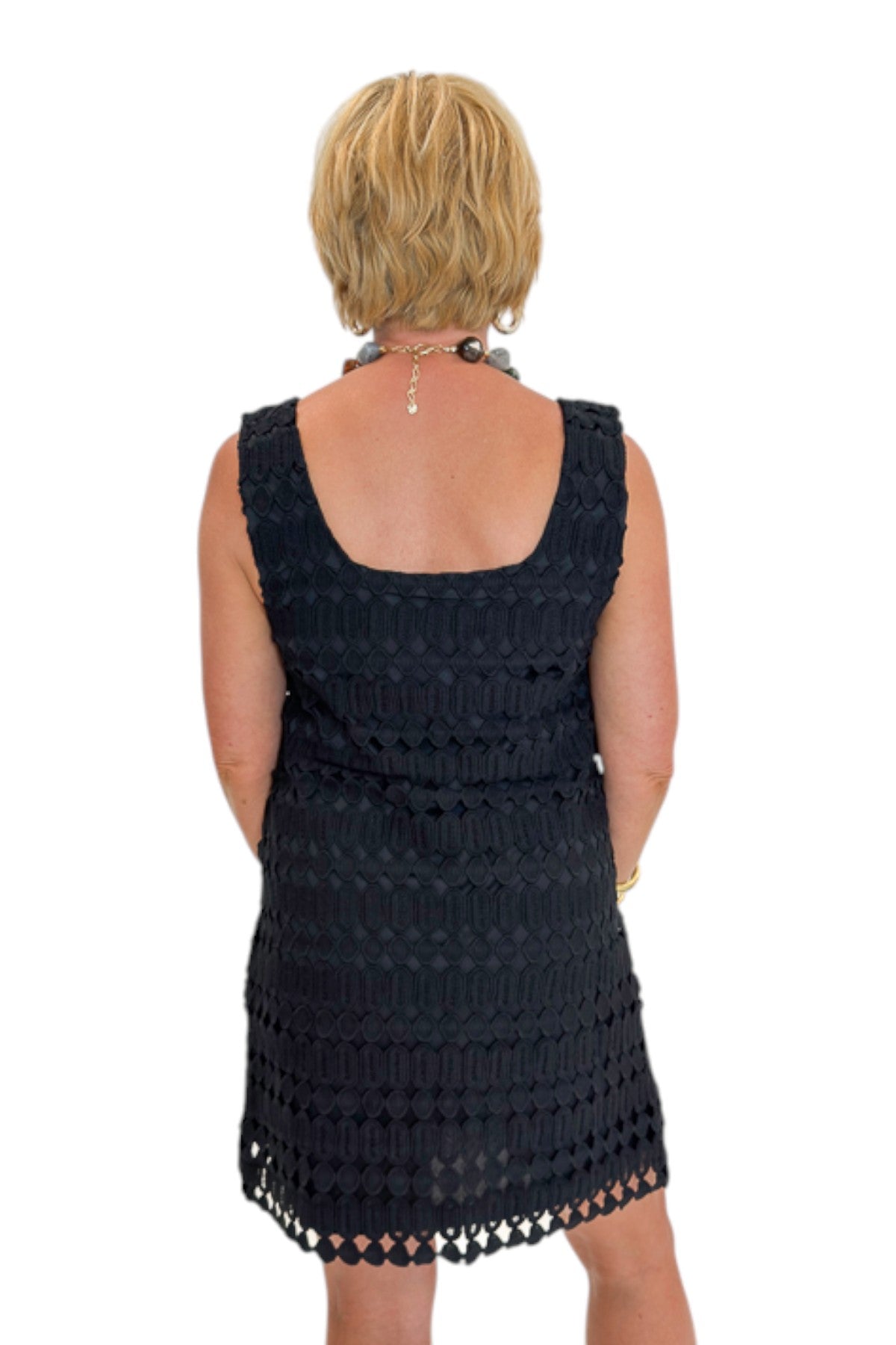 Back view of woman wearing Swagger Boutique’s Black Sleeveless Lace Mini Dress by Entro with heels against white studio background.