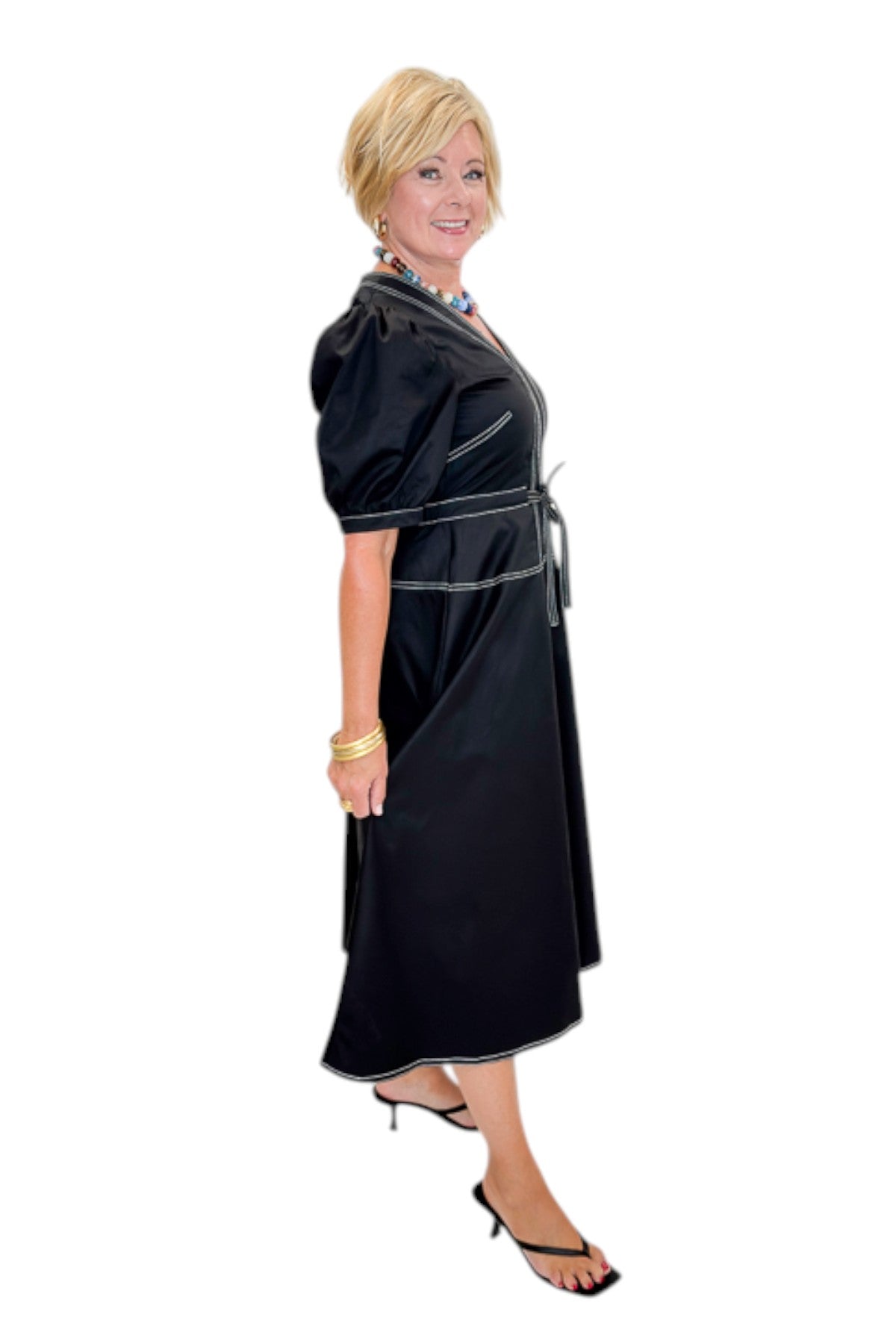 Side view of woman wearing Swagger Boutique’s Black Stitch Midi Dress with heels against white studio background.