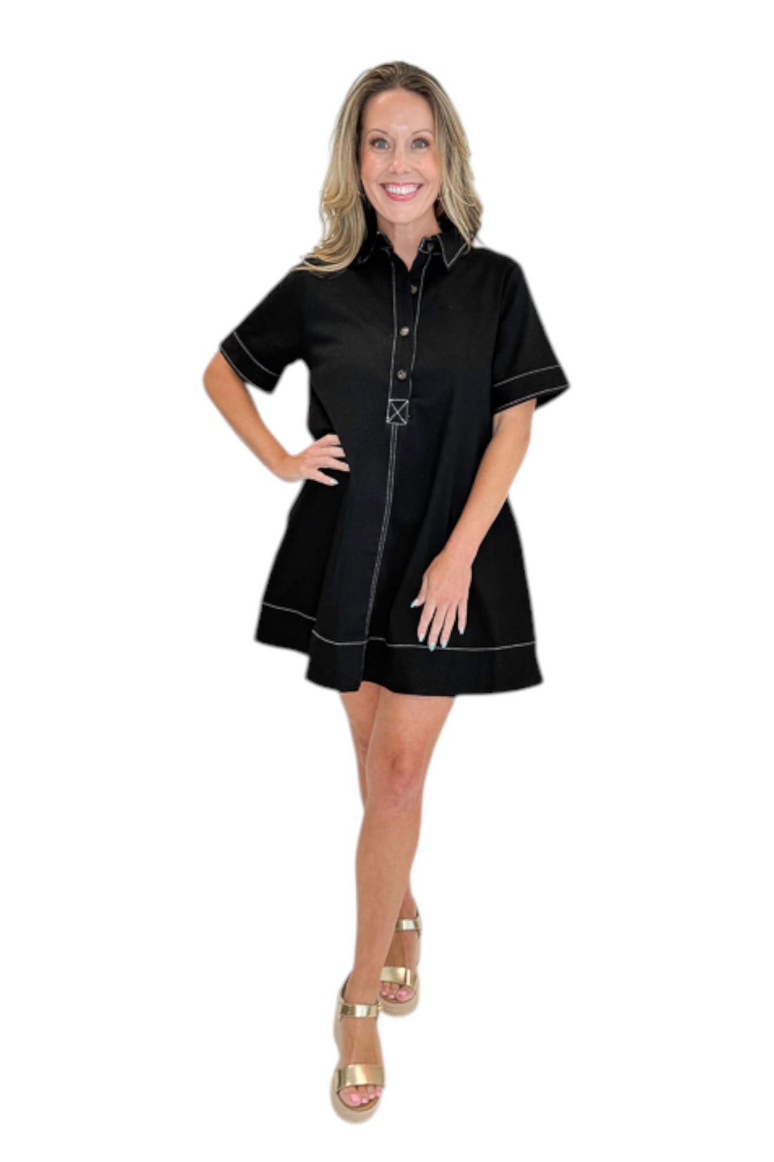 Front view of woman wearing Swagger Boutique’s Black Stitched Mini Dress with gold wedges against a white studio background. 