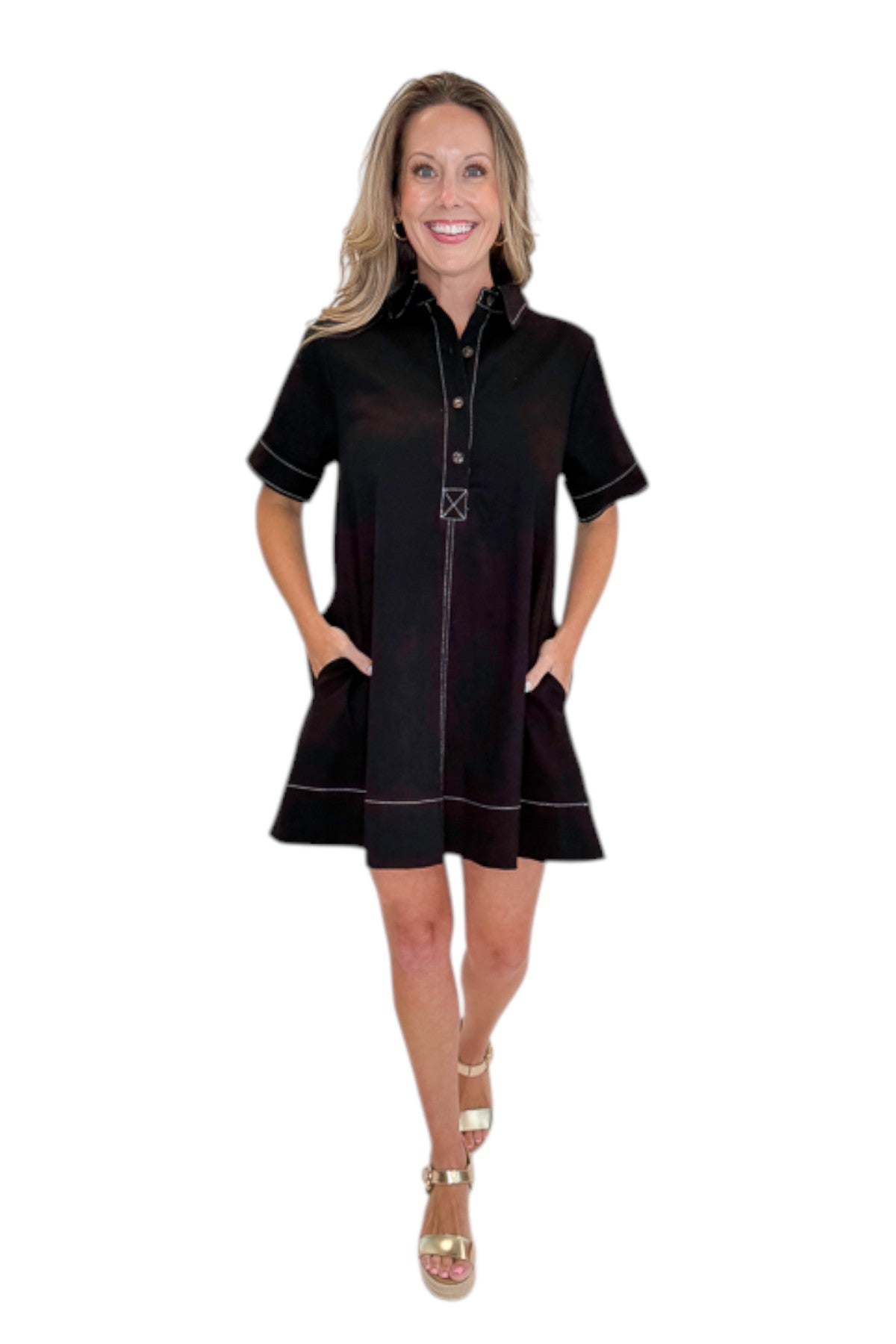 Front view of woman wearing Swagger Boutique’s Black Stitched Mini Dress with gold wedges against a white studio background. 