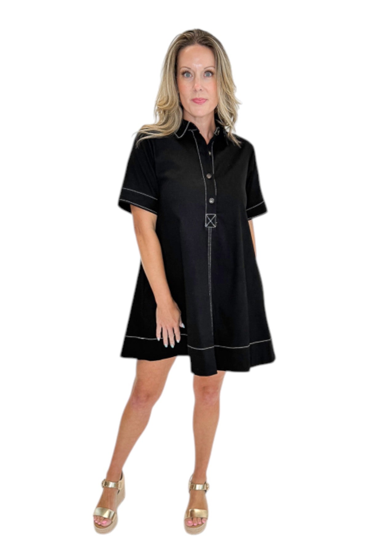 Front view of woman wearing Swagger Boutique’s Black Stitched Mini Dress with gold wedges against a white studio background. 