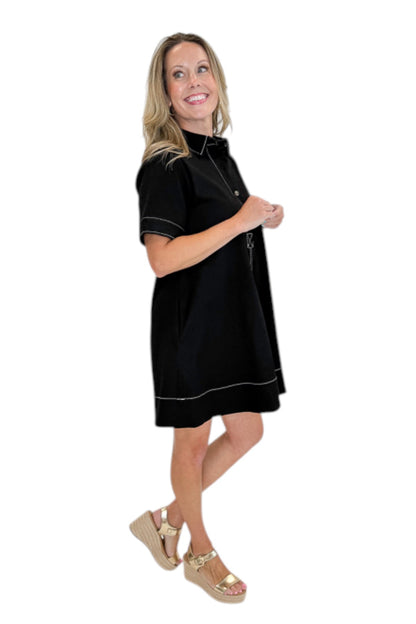 side view of woman wearing Swagger Boutique’s Black Stitched Mini Dress with tan wedges against a white studio background. 