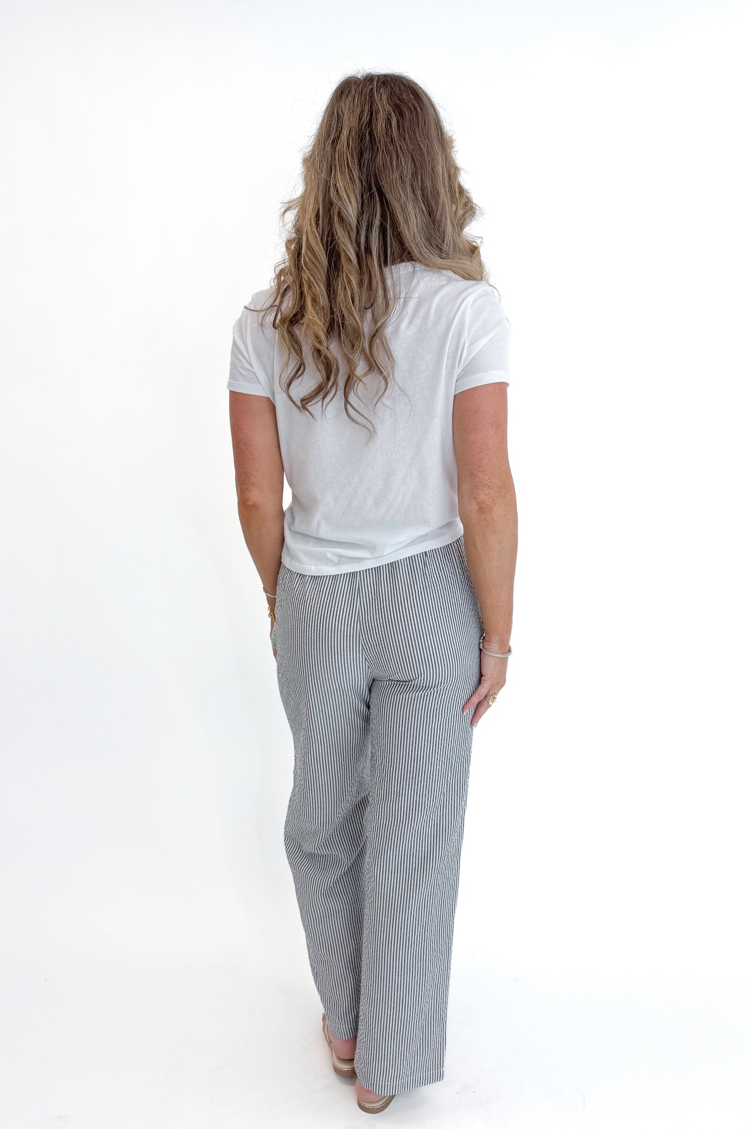 Back view of woman wearing Swagger Boutique’s Black Striped Wide Leg Pants with Junie White Tee by Z Supply against white studio background.