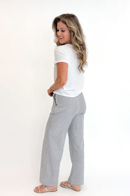 Side view of woman wearing Swagger Boutique’s Black Striped Wide Leg Pants with Junie White Tee by Z Supply against white studio background.