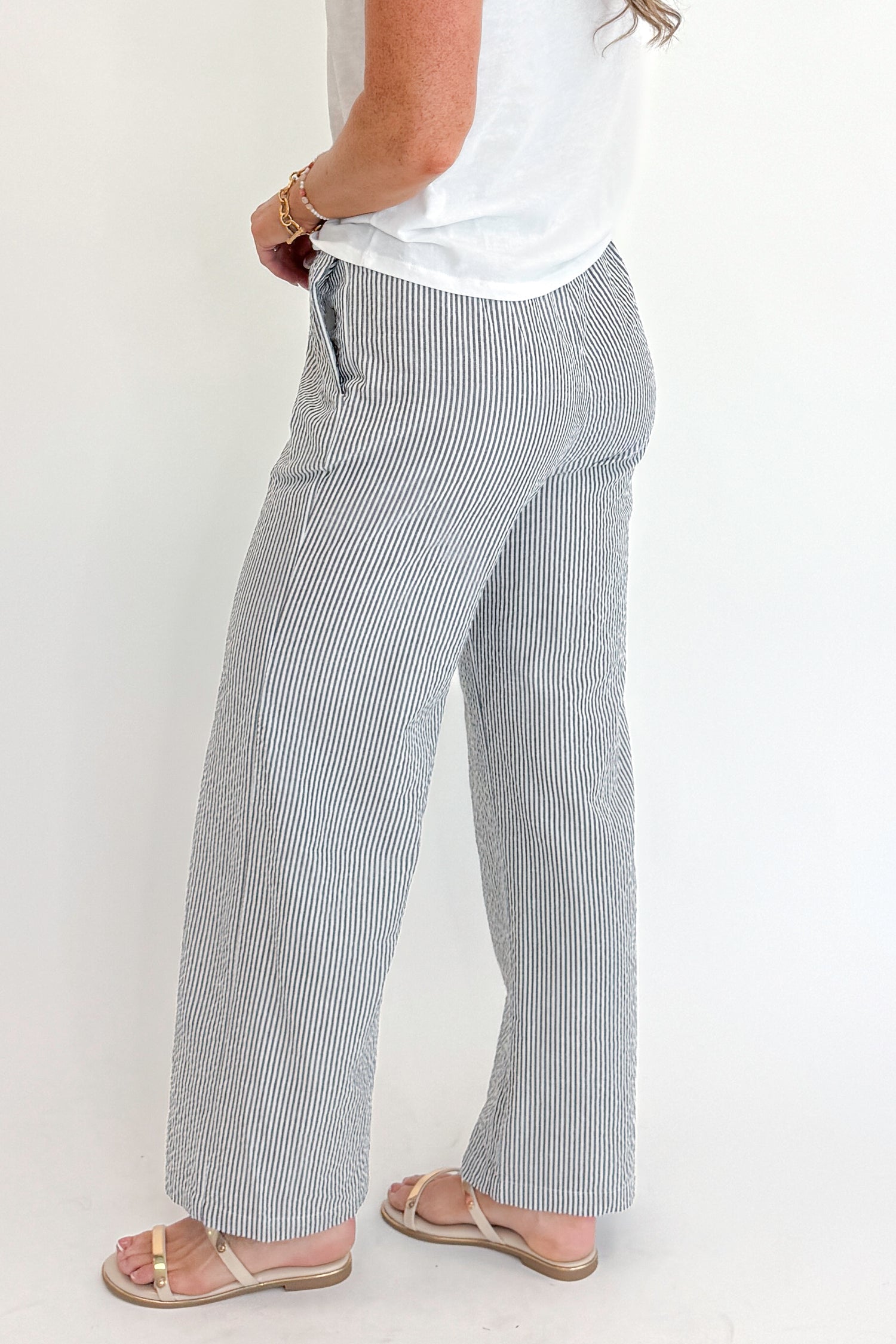Side detail view of woman wearing Swagger Boutique’s Black Striped Wide Leg Pants with Junie White Tee by Z Supply against white studio background.