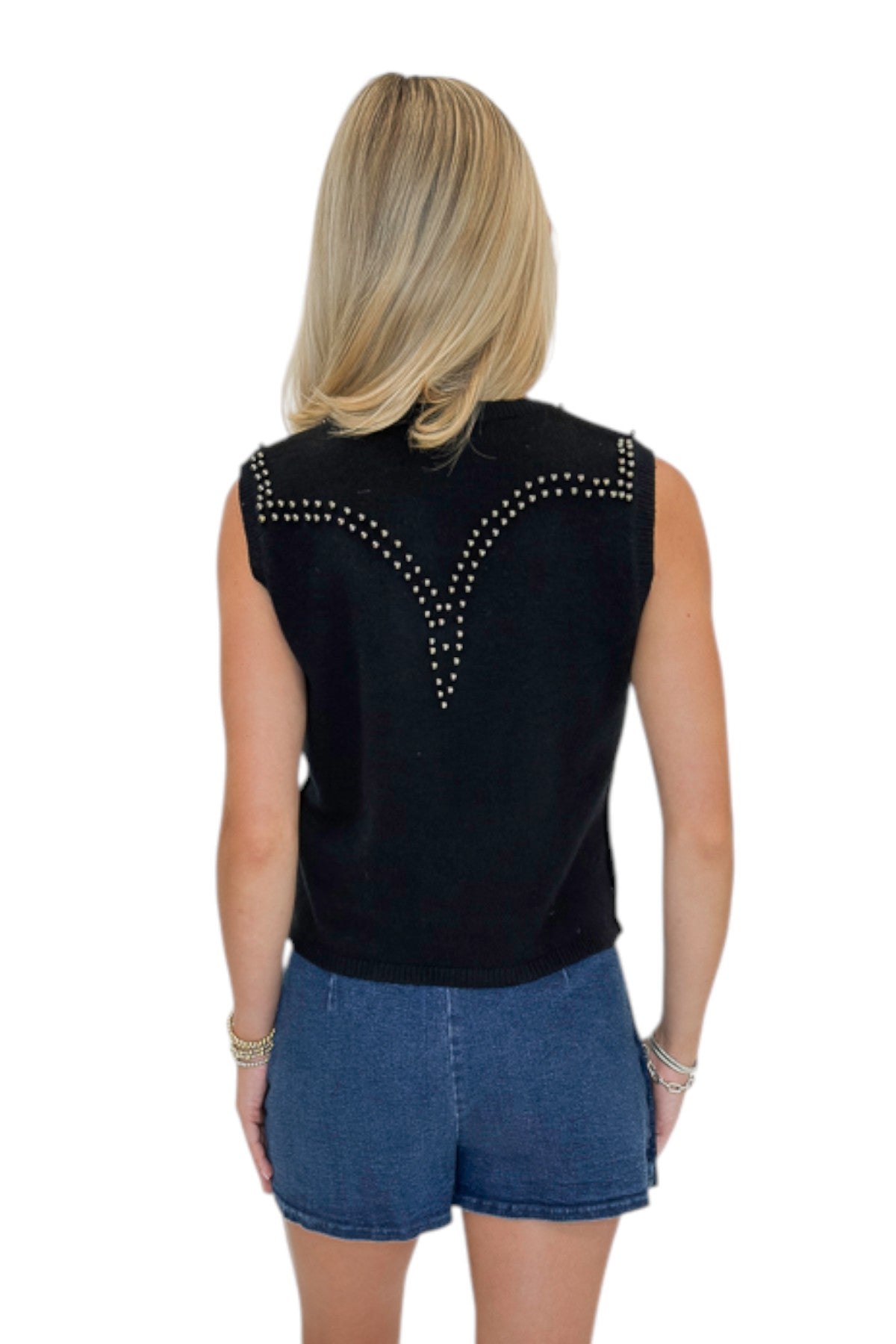 Back view of woman wearing Swagger Boutique’s Black Studded Sweater Vest with Dark Wash Studded Denim Skort against white studio background.