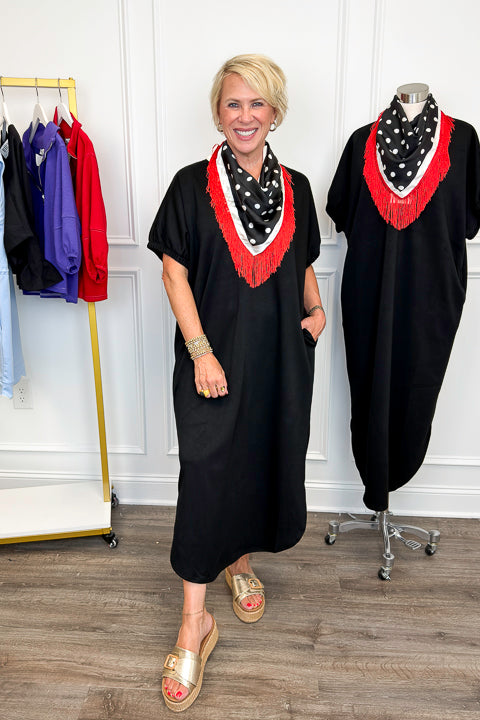 Front view of woman wearing Swagger Boutique’s Black With Cream Lining Midi Dress with sandals with clothing hanging in the background. 