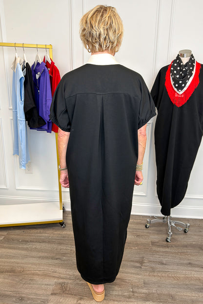 Back view of woman wearing Swagger Boutique’s Black With Cream Lining Midi Dress with sandals with clothing hanging in the background. 
