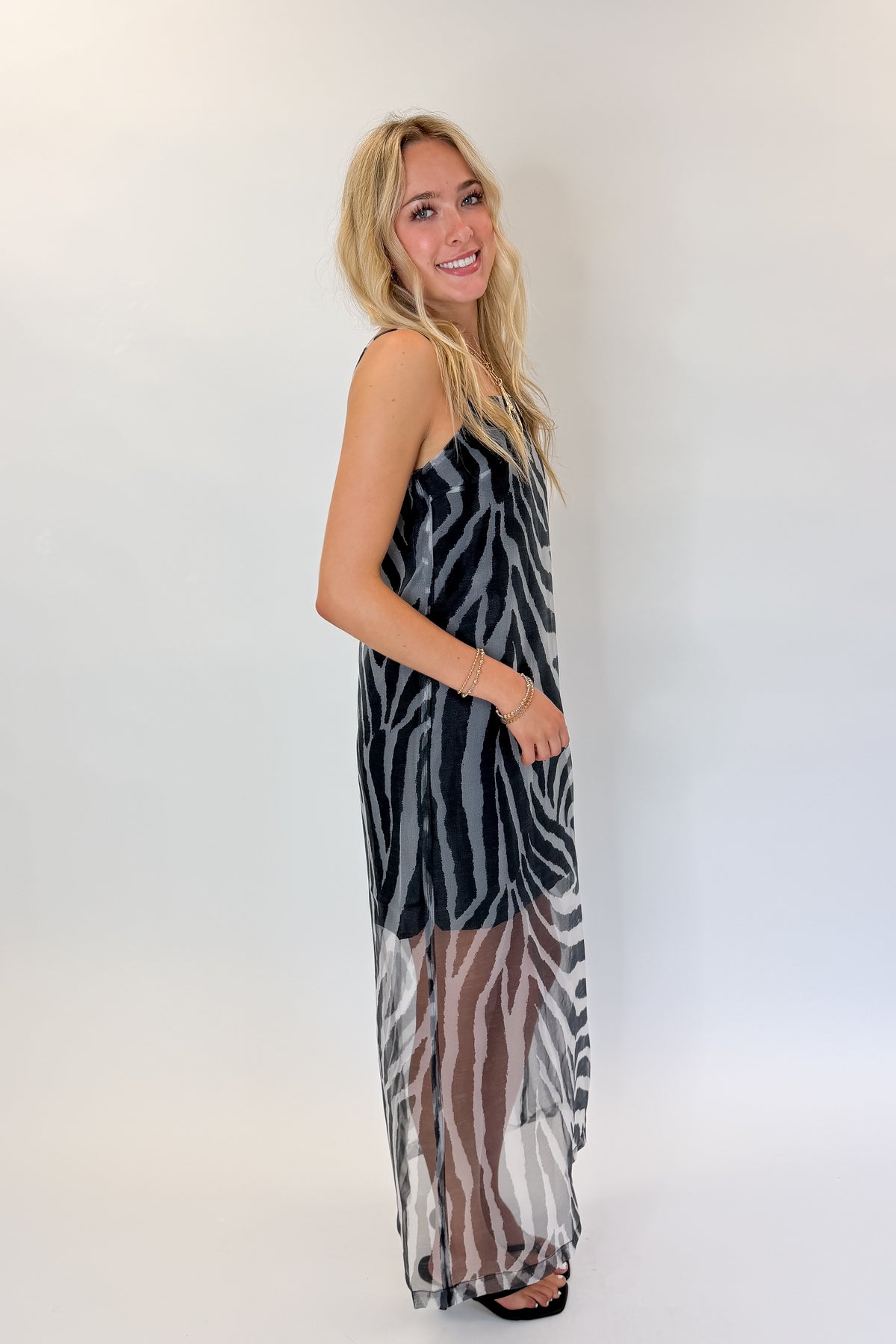Side view of woman wearing Swagger Boutique’s Black Zebra Maxi Dress with heels against white studio background.
