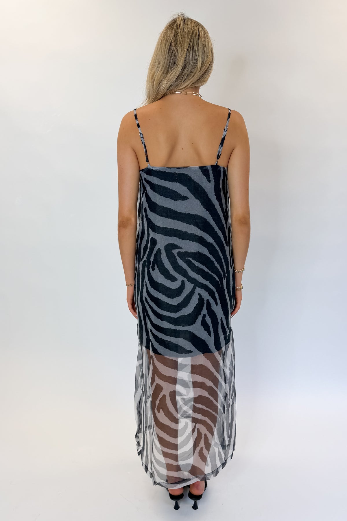 Back view of woman wearing Swagger Boutique’s Black Zebra Maxi Dress with heels against white studio background.