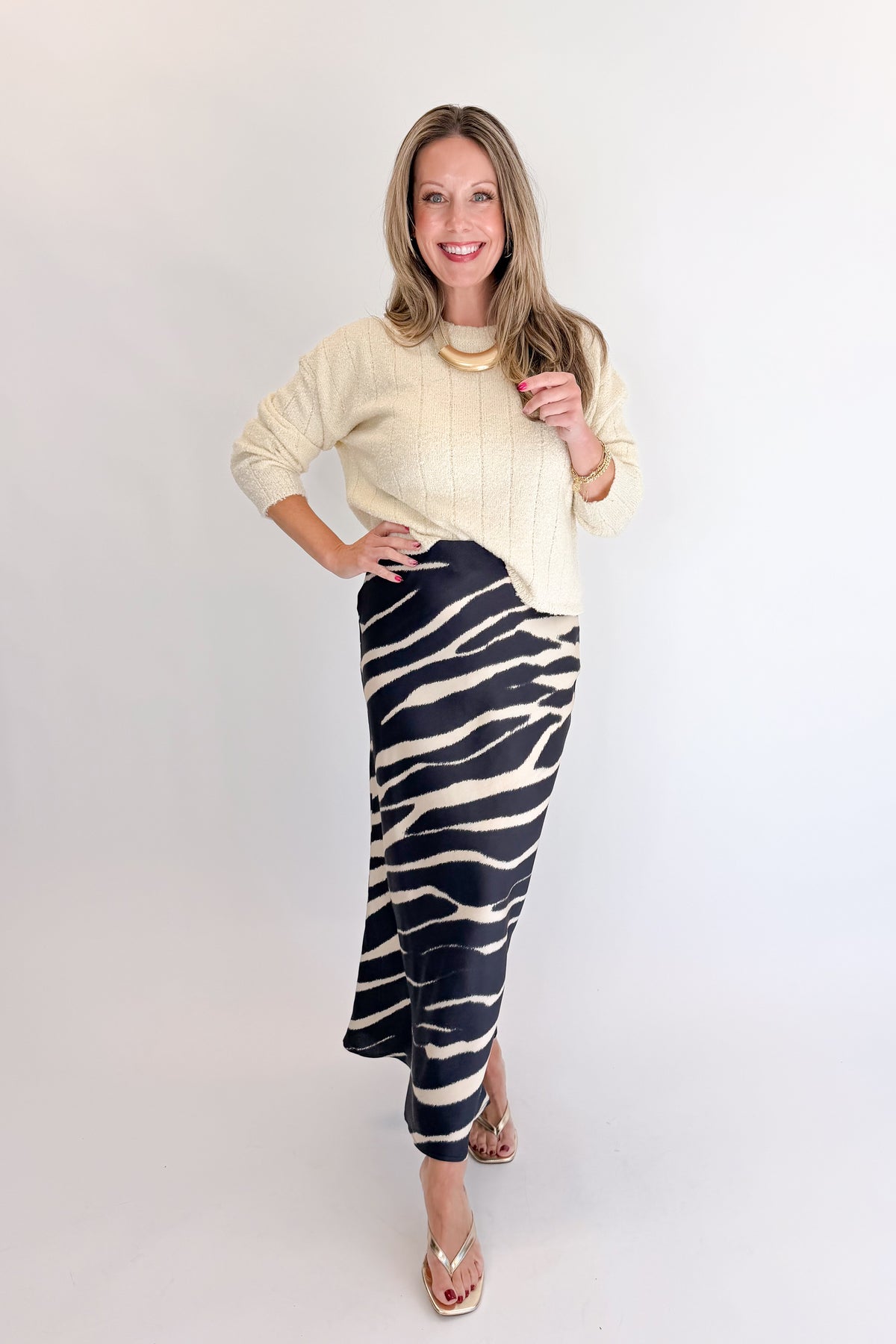 Front view of woman wearing Swagger Boutique’s Black Zebra Print Satin Skirt with Cream Ribbed Textured Sweater against white studio background.