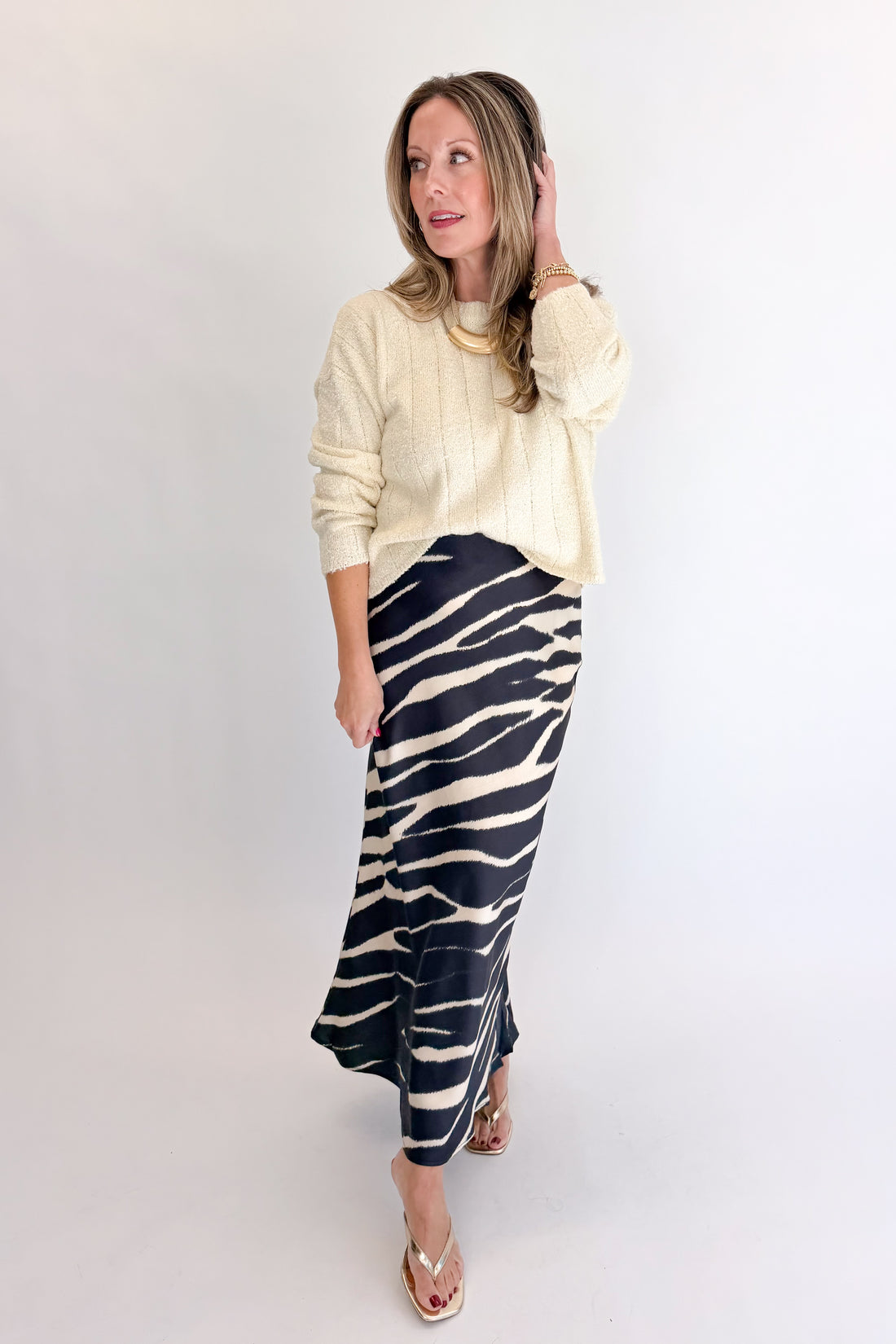 Front view of woman wearing Swagger Boutique’s Black Zebra Print Satin Skirt with Cream Ribbed Textured Sweater against white studio background.