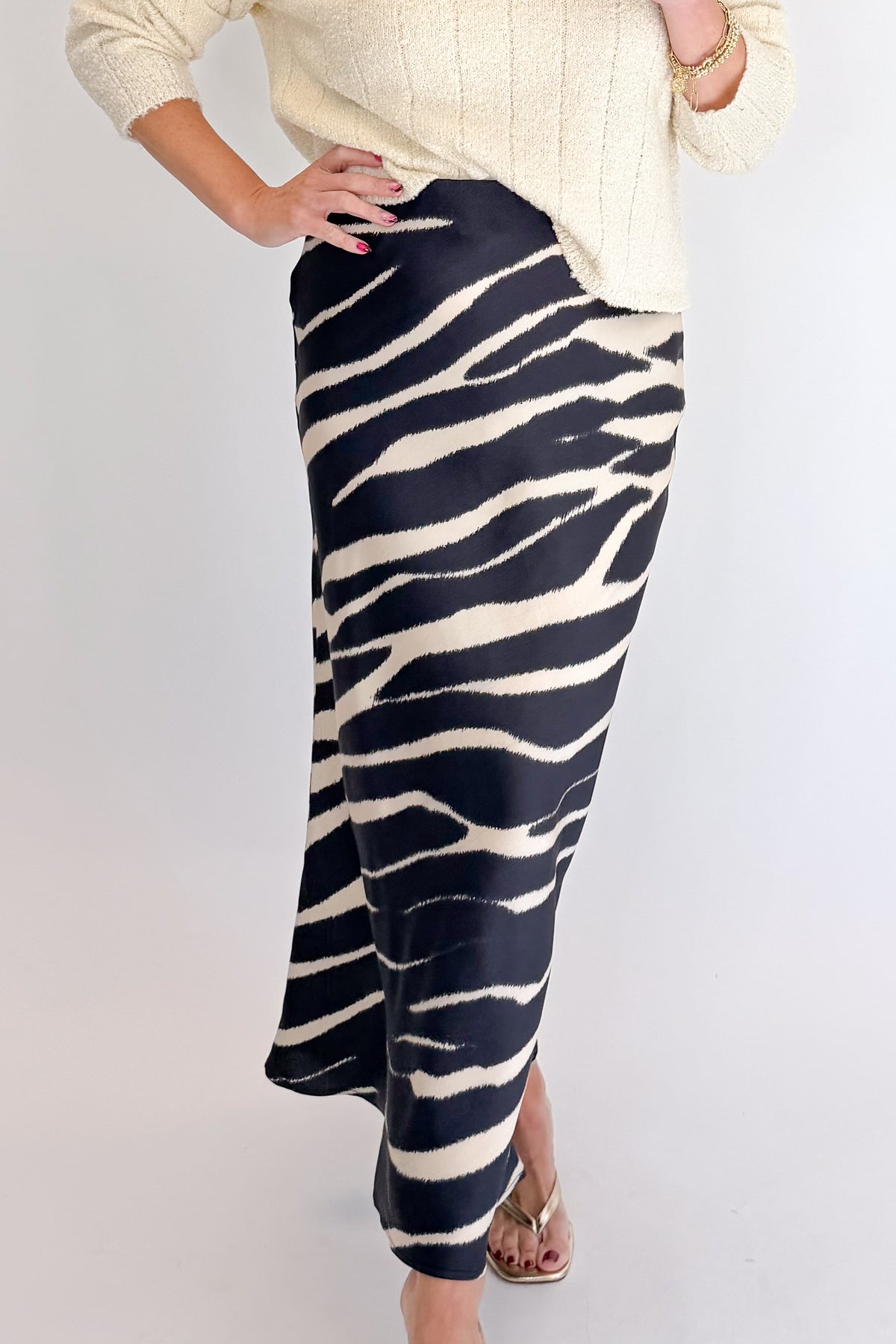 Front detail view of woman wearing Swagger Boutique’s Black Zebra Print Satin Skirt with Cream Ribbed Textured Sweater against white studio background.
