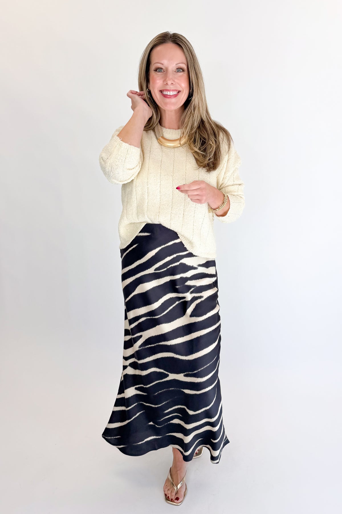 Front view of woman wearing Swagger Boutique’s Black Zebra Print Satin Skirt with Cream Ribbed Textured Sweater against white studio background.