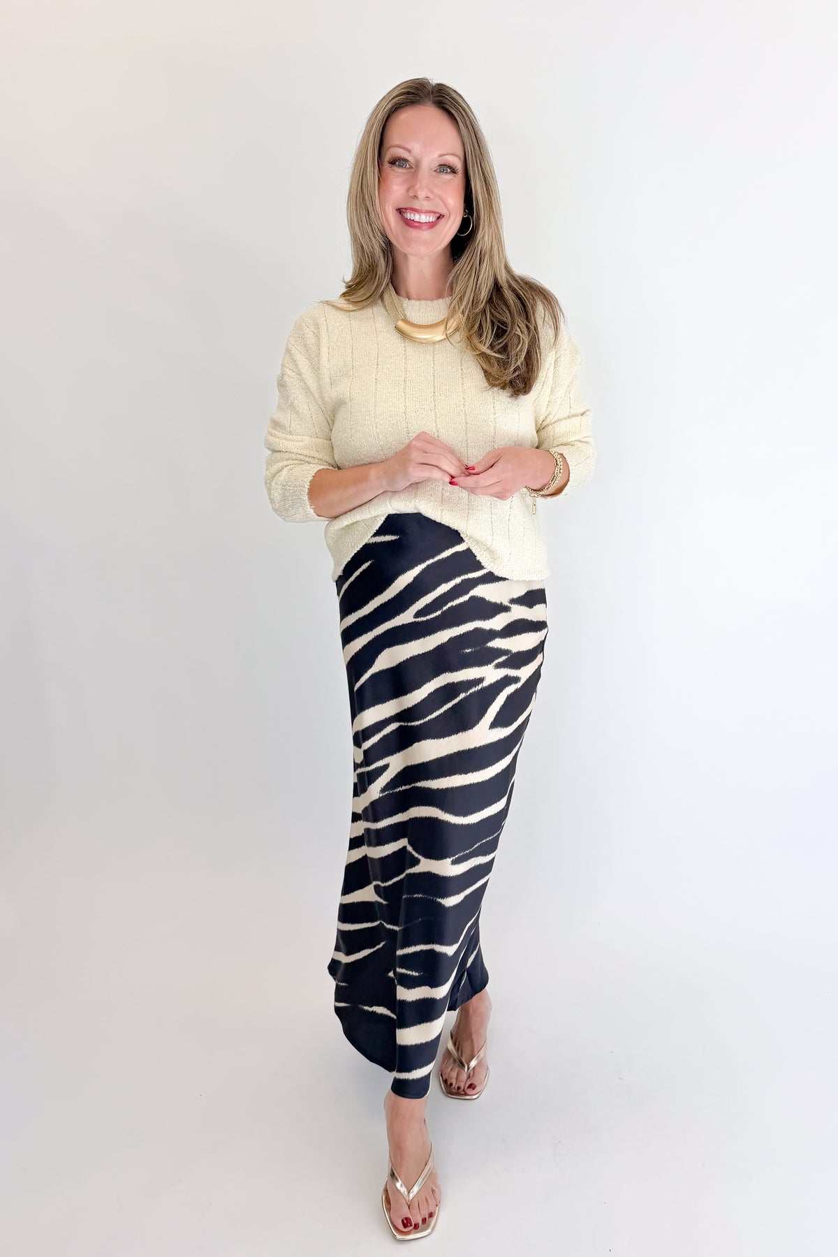 Front view of woman wearing Swagger Boutique’s Black Zebra Print Satin Skirt with Cream Ribbed Textured Sweater against white studio background.
