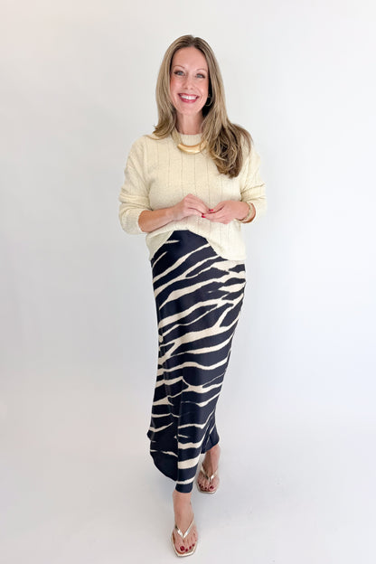Front view of woman wearing Swagger Boutique’s Black Zebra Print Satin Skirt with Cream Ribbed Textured Sweater against white studio background.