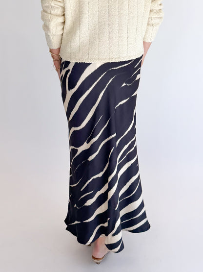 Back detail view of woman wearing Swagger Boutique’s Black Zebra Print Satin Skirt with Cream Ribbed Textured Sweater against white studio background.
