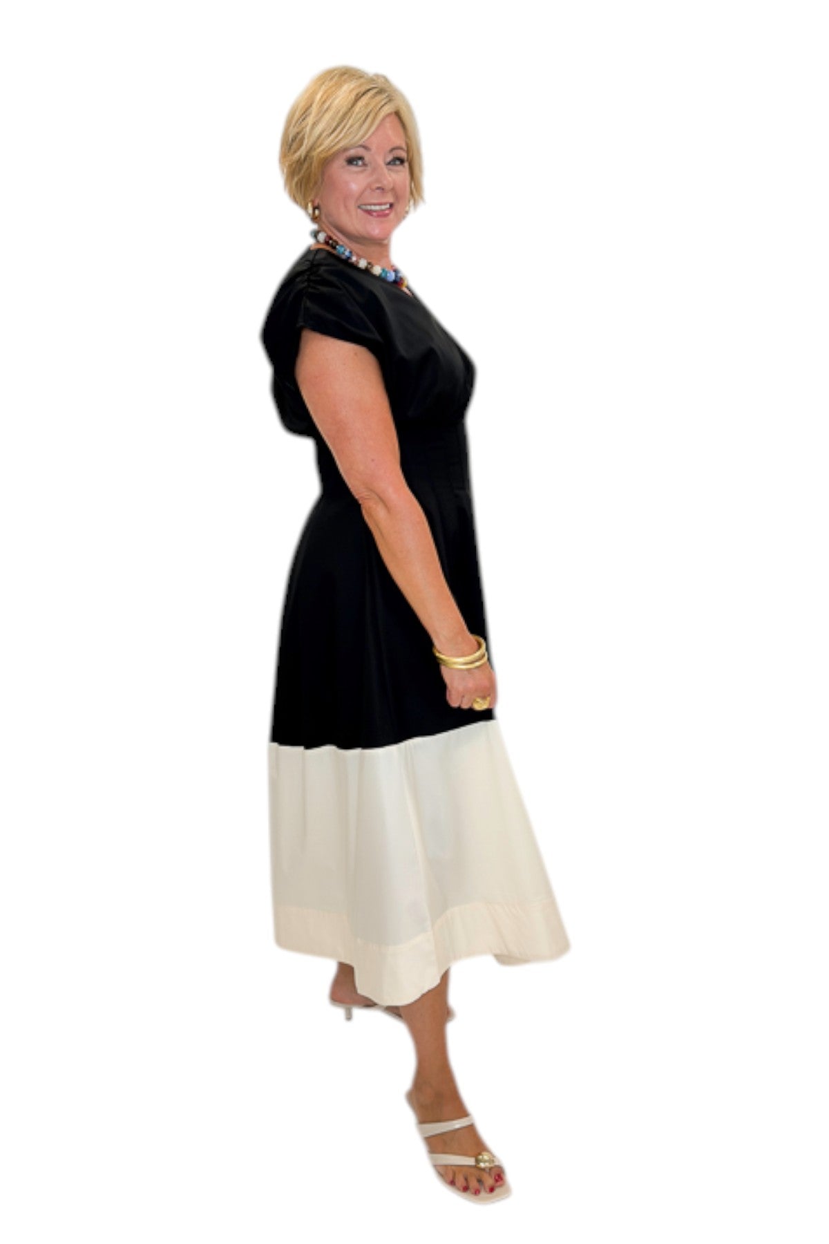 Side view of woman wearing Swagger Boutique’s Black &amp; Cream Color Block Midi Dress by Entro with sandals against white studio background.