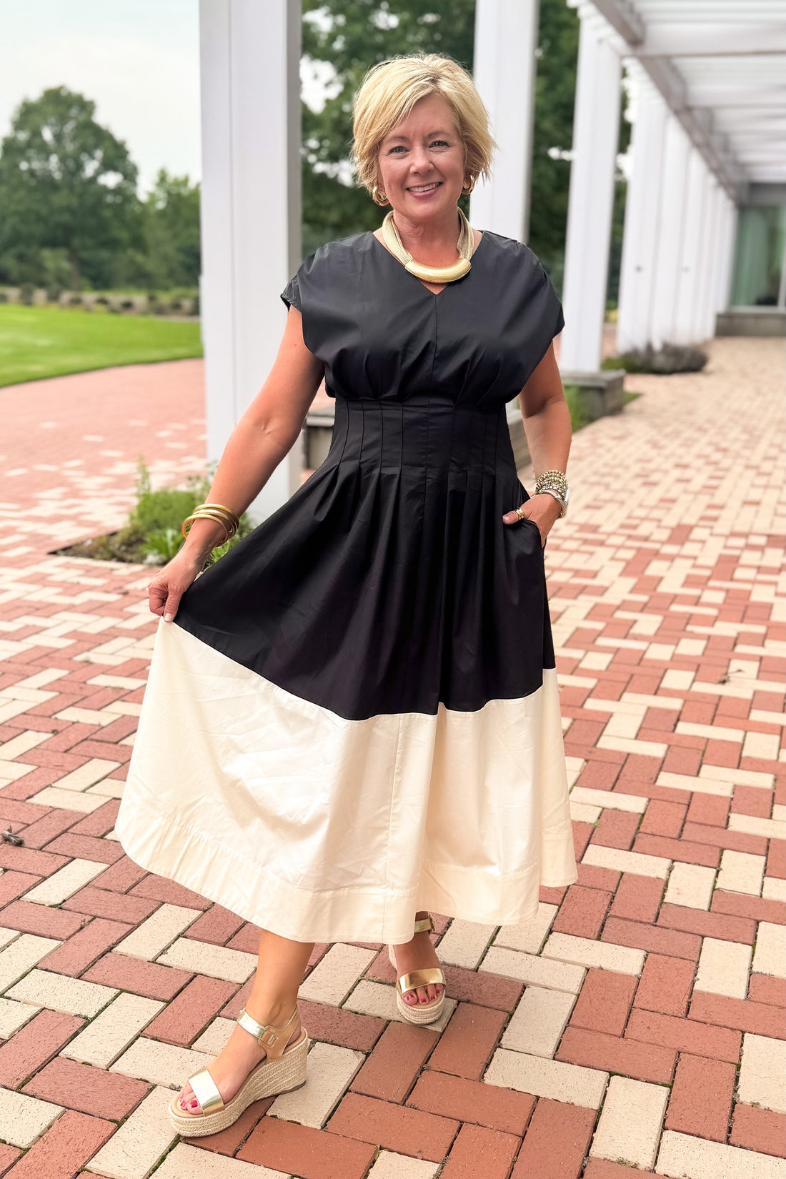 Front view of woman wearing Swagger Boutique’s Black &amp; Cream Color Block Midi Dress by Entro with sandals walking down a brick walkway outside.