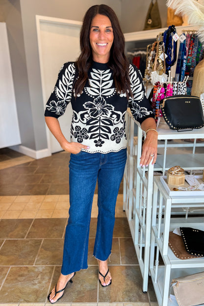 Front view of woman wearing Swagger Boutique’s Black &amp; Cream Printed Short Sleeve Sweater by THML with jeans standing at the store.