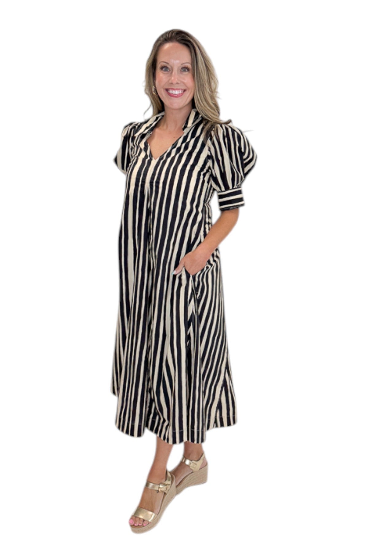 Side view of woman wearing Swagger Boutique’s Black &amp; Cream Striped Midi Dress with sandals against white studio background.