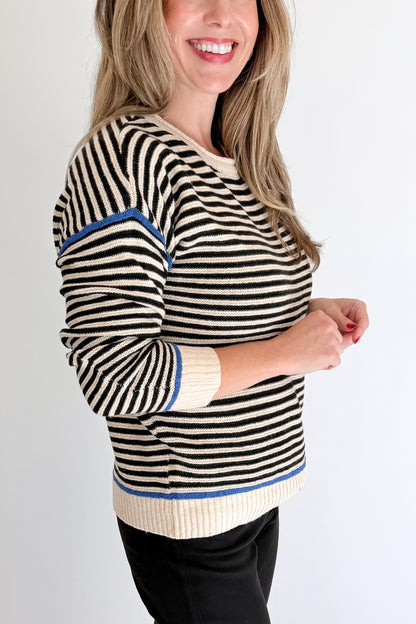 Side detail view of woman wearing Swagger Boutique’s Black &amp; Cream Striped Sweater With Blue Accent with Kelsey Black Jeans against white studio background.