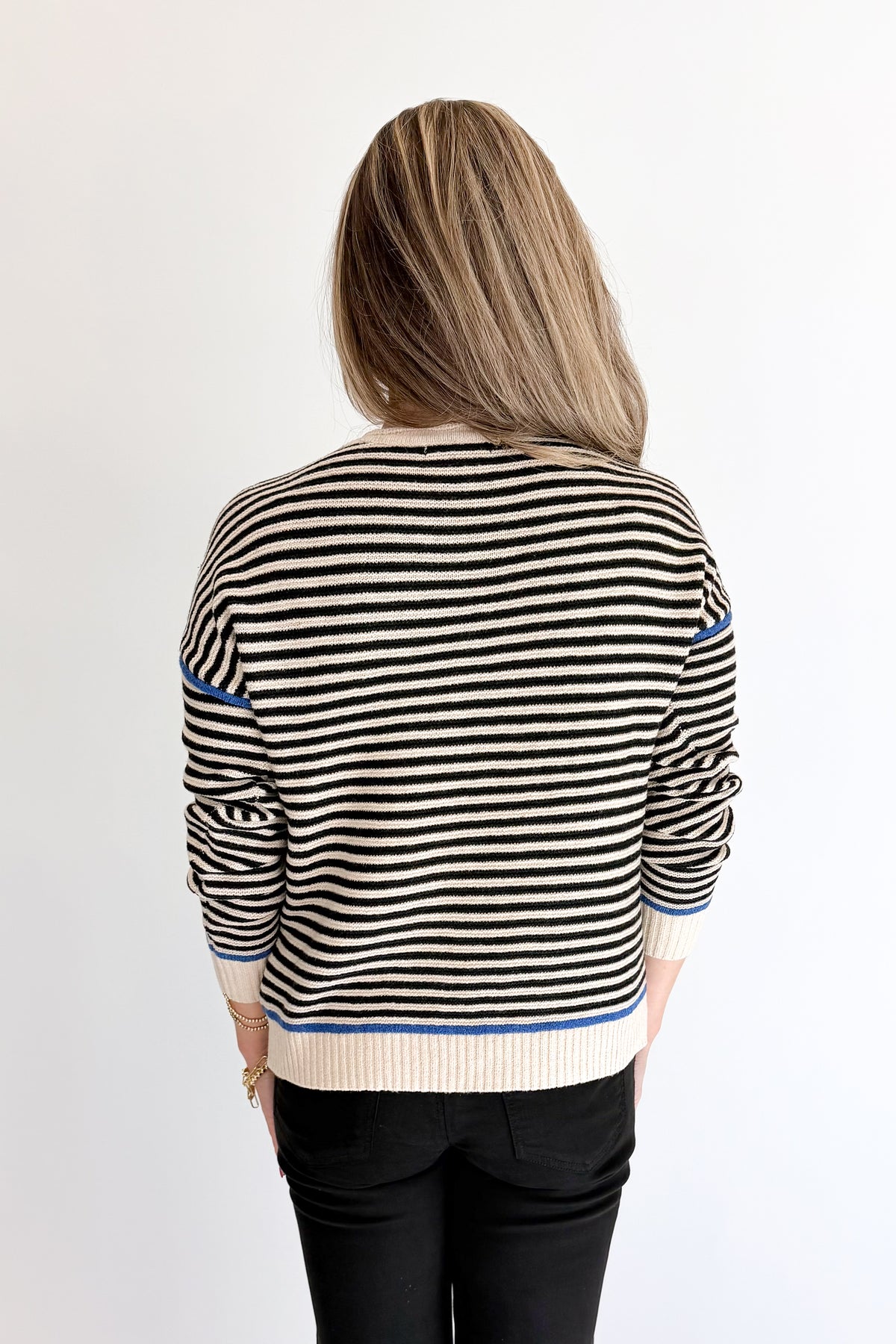 Back view of woman wearing Swagger Boutique’s Black &amp; Cream Striped Sweater With Blue Accent with Kelsey Black Jeans against white studio background.