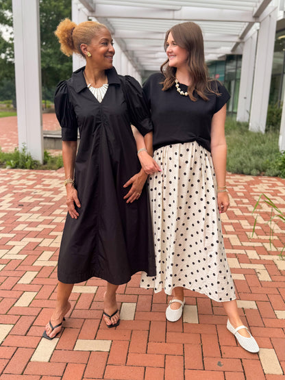 Front view of women wearing Swagger Boutique’s Black &amp; Cream Polka Dot Layered Midi Dress by Entro and Black Collared Midi Dress outside by a red brick walkway.