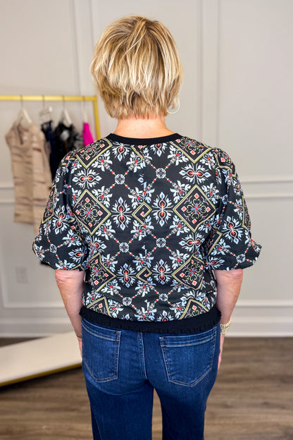 Back view of woman wearing Swagger Boutique’s Black Embroidered Print Top with jeans with clothing hanging in the background.