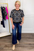 Front view of woman wearing Swagger Boutique’s Black Embroidered Print Top with jeans with clothing hanging in the background.