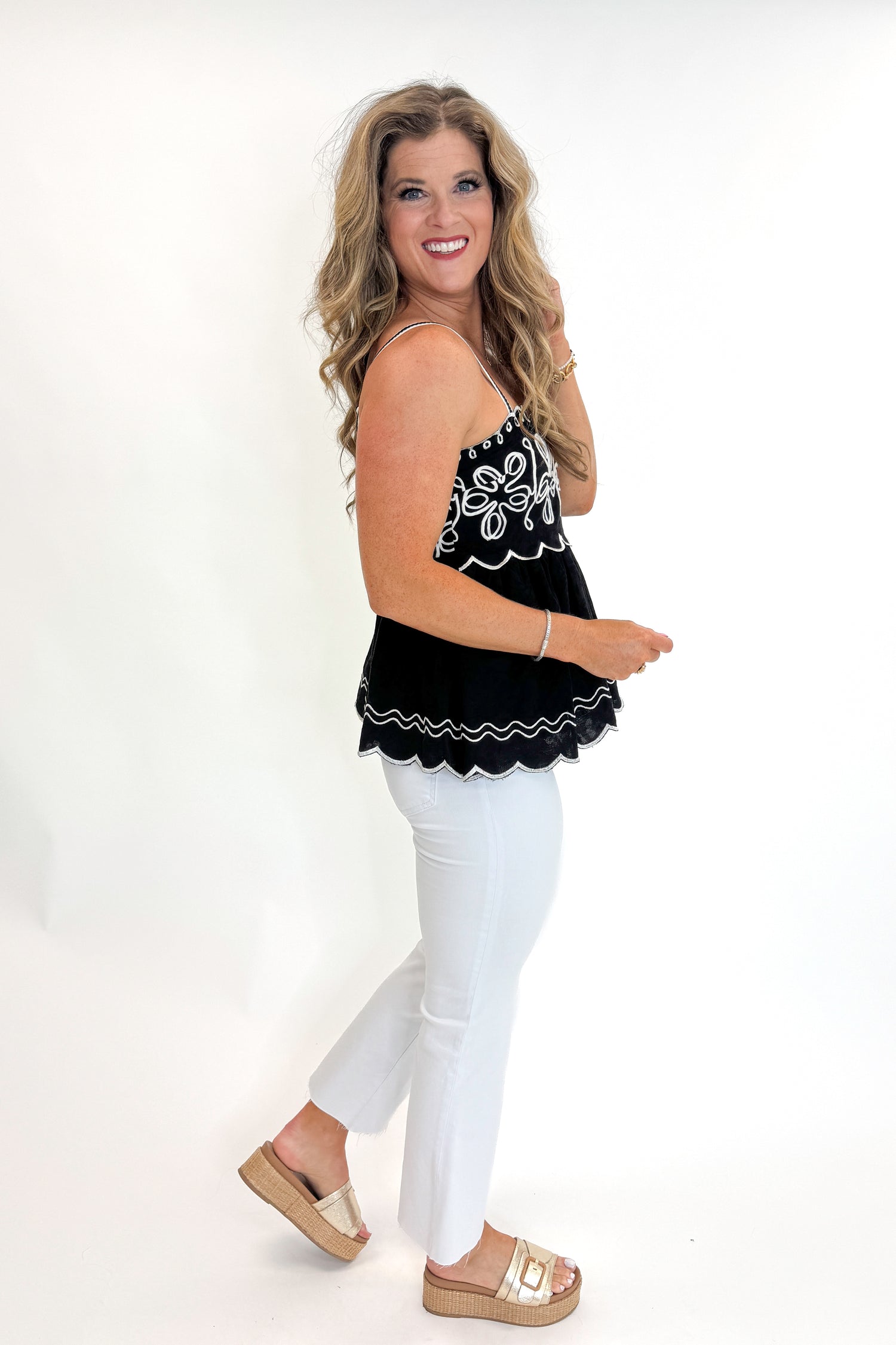 Side view of woman wearing Swagger Boutique’s Black &amp; Ivory Embroidered Tank with jeans against white studio background.