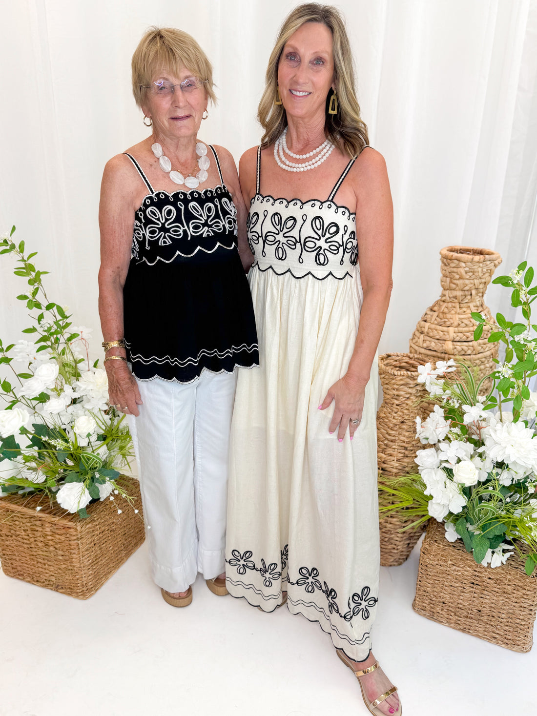 Front view of woman wearing Swagger Boutique’s Black &amp; Ivory Embroidered Tank with jeans with daughter wearing Cream &amp; Black Embroidered Maxi Dress against white studio background.