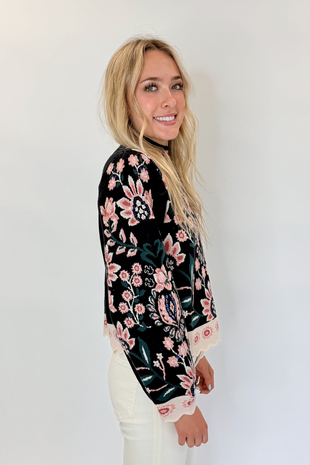 Side view of woman wearing Swagger Boutique’s Black &amp; Multi Floral Print Sweater by THML with jeans against white studio background.