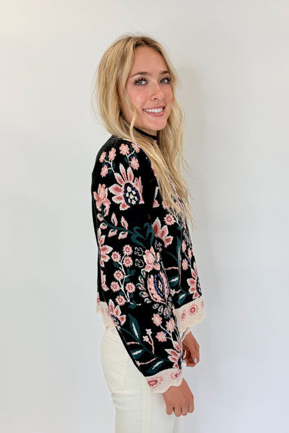 Side view of woman wearing Swagger Boutique’s Black &amp; Multi Floral Print Sweater by THML with jeans against white studio background.