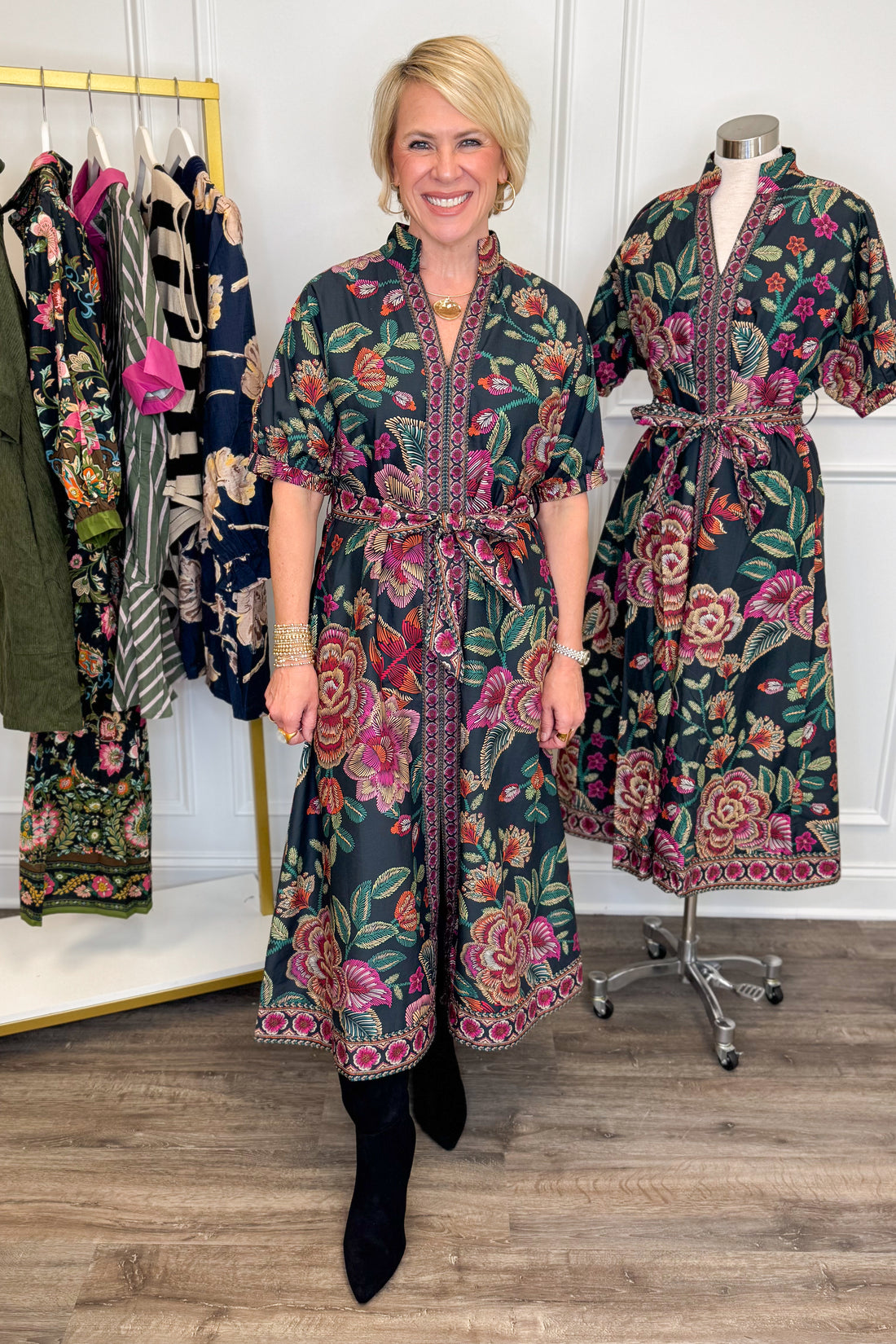 Front view of woman wearing Swagger Boutique’s Black &amp; Multi Printed 3/4 Sleeve Midi Dress by Entro with boots with clothing hanging in the background.