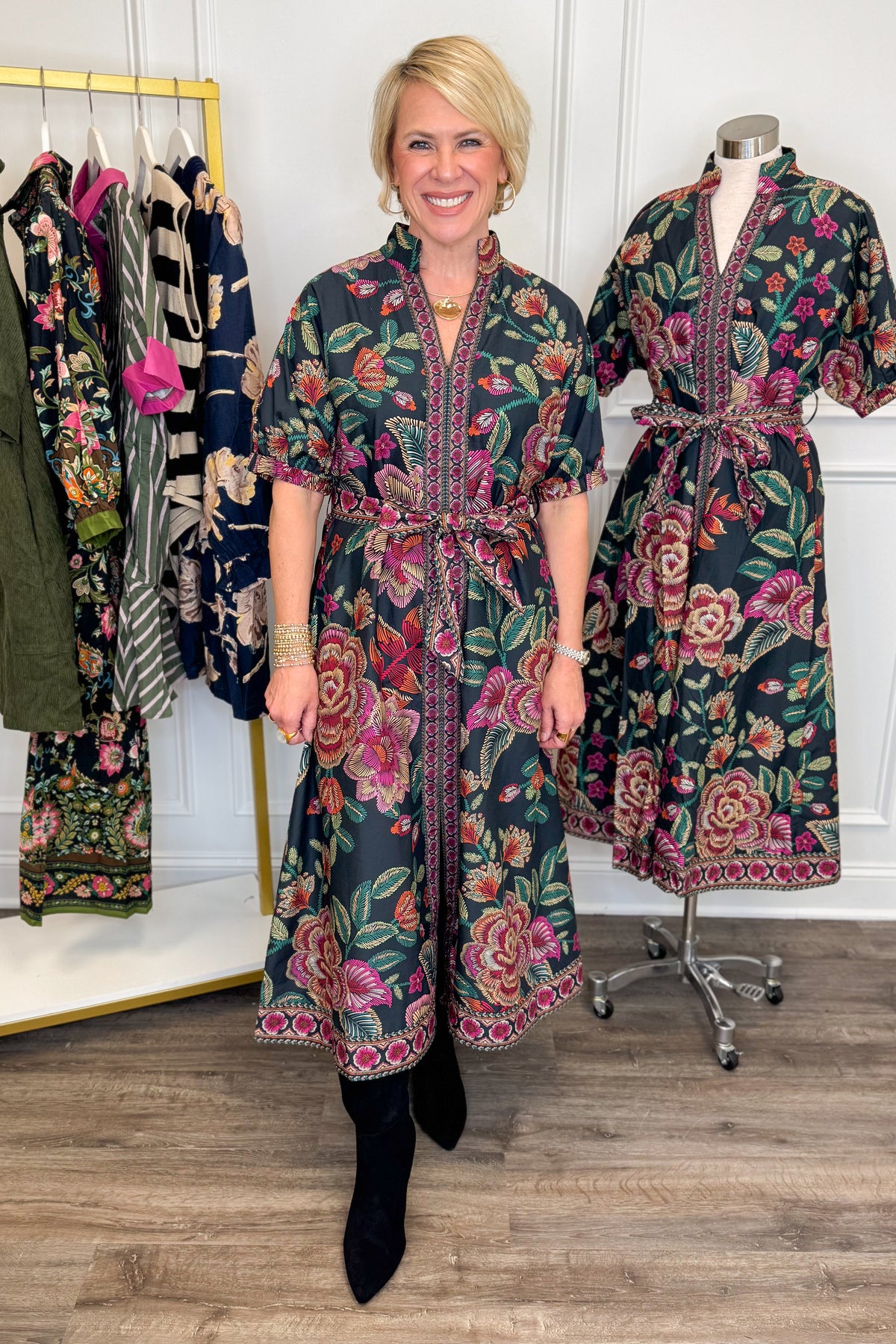 Front view of woman wearing Swagger Boutique’s Black &amp; Multi Printed 3/4 Sleeve Midi Dress by Entro with boots with clothing hanging in the background.
