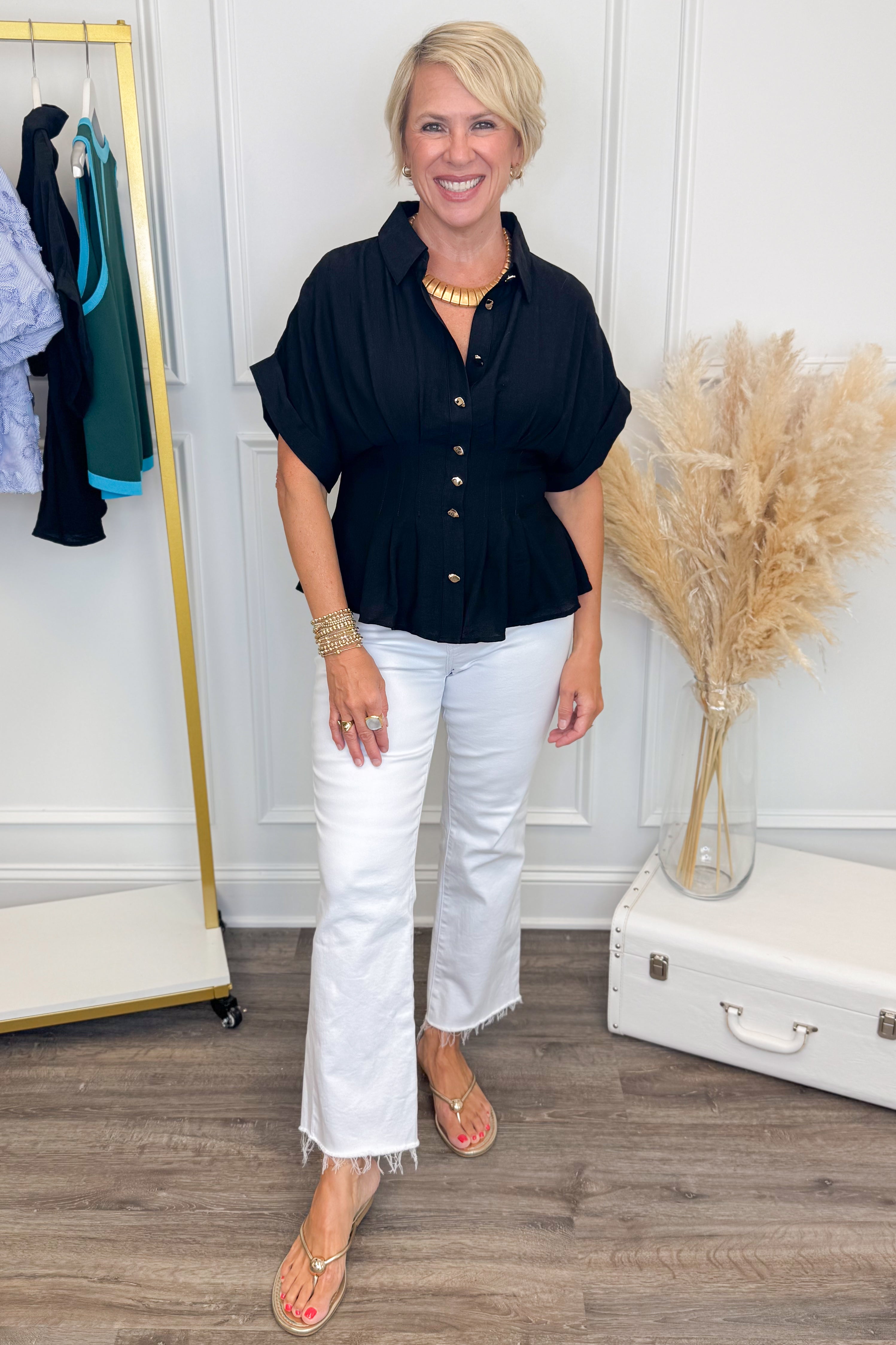 front view of woman wearing a navy short sleeve collared top with white shorts and sandals with white studio background 
