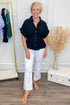 front view of woman wearing a navy short sleeve collared top with white shorts and sandals with white studio background 
