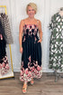 Front view of woman wearing Swagger Boutique’s Black & Red Floral Midi Dress by Entro with sandals with clothing hanging in the background. 
