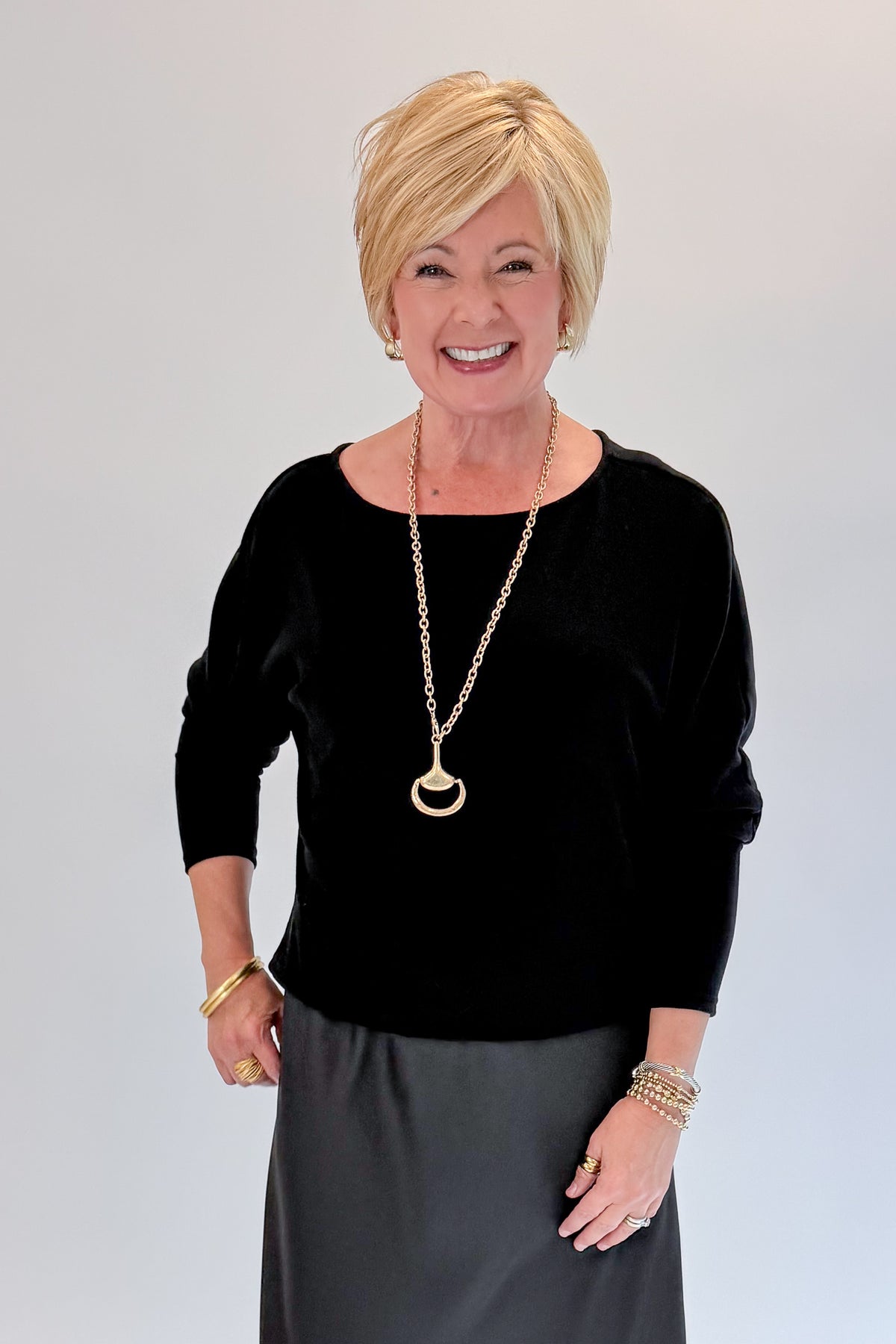 Front view of woman wearing Swagger Boutique’s Black Satin Dress and Black Layering Sweater with heels against white studio background.