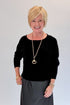 Front view of woman wearing Swagger Boutique’s Black Satin Dress and Black Layering Sweater with heels against white studio background.