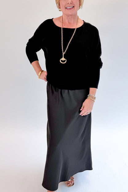 Front detail view of woman wearing Swagger Boutique’s Black Satin Dress and Black Layering Sweater with heels against white studio background.