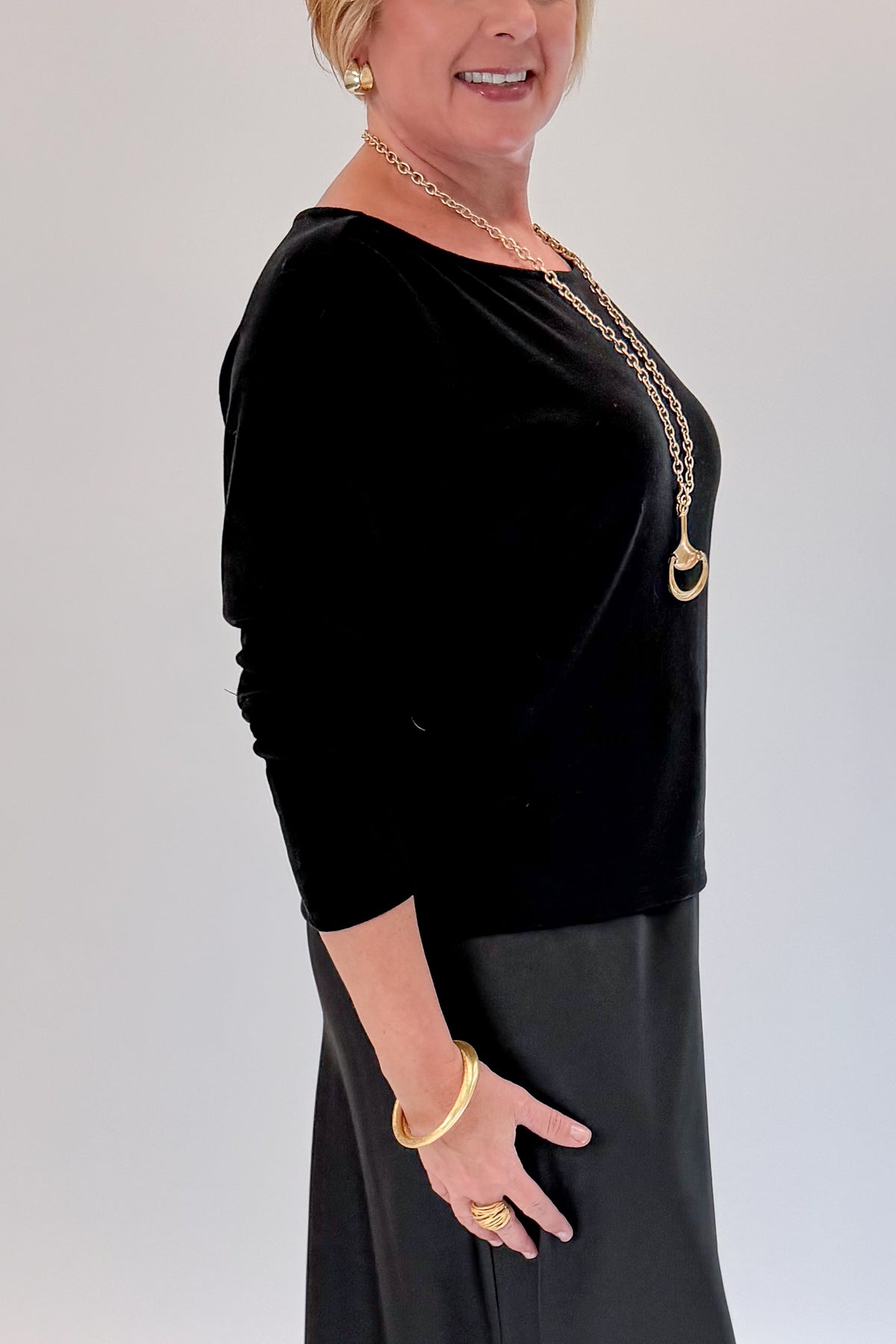 Side detail view of woman wearing Swagger Boutique’s Black Satin Dress and Black Layering Sweater with heels against white studio background.