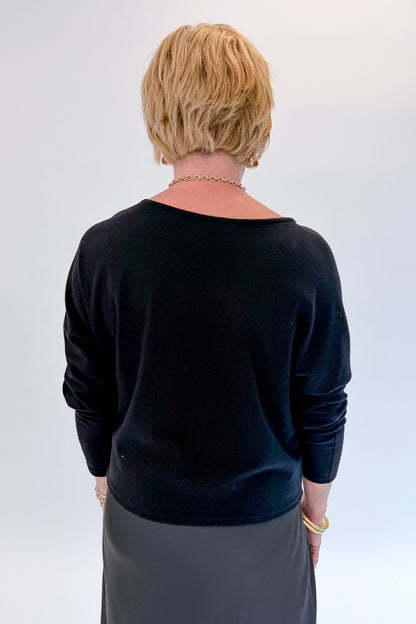 Back view of woman wearing Swagger Boutique’s Black Satin Dress and Black Layering Sweater with heels against white studio background.