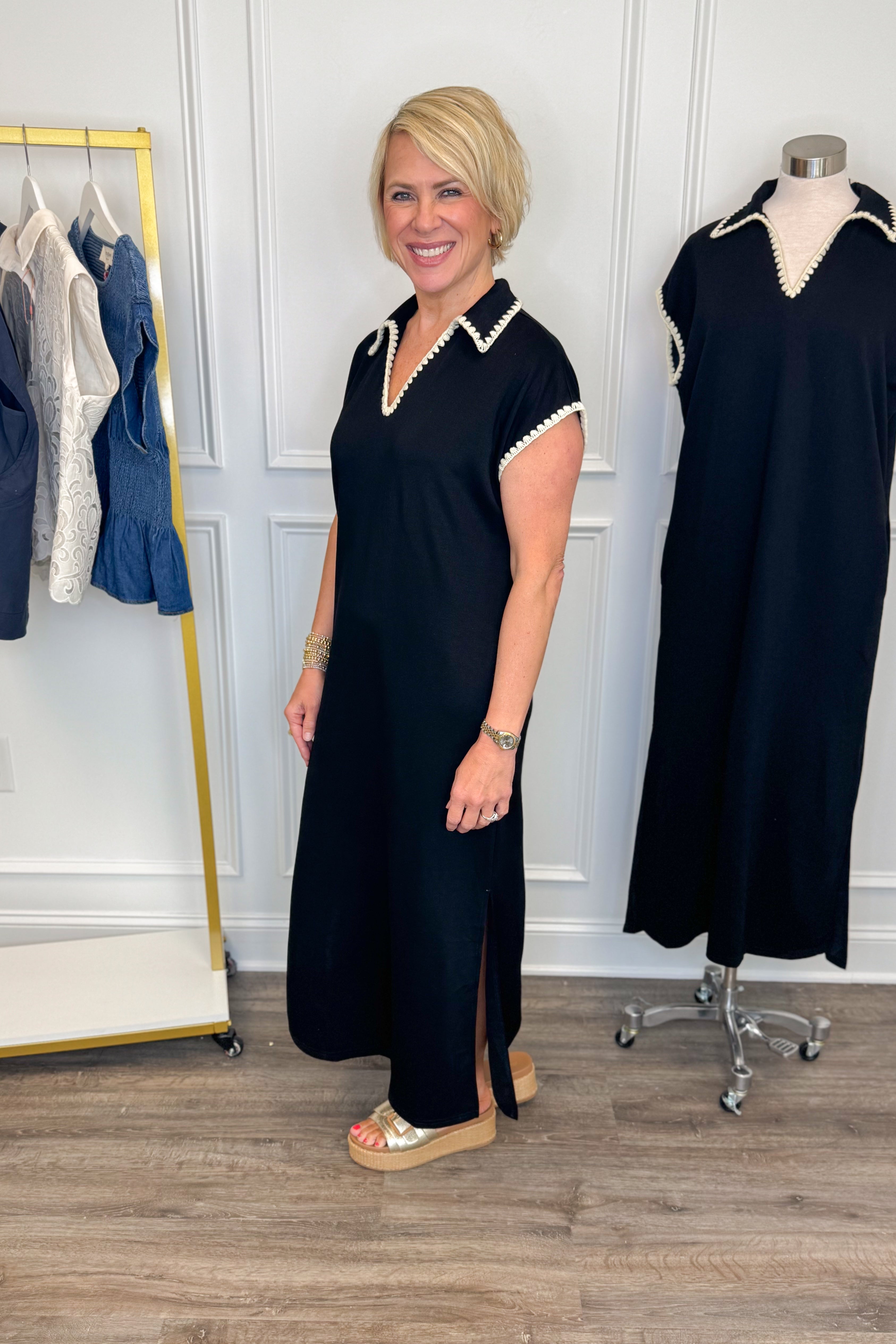 Side view of woman wearing Swagger Boutique’s Black Whipstitch Midi Dress by Entro with sandals with clothing hanging in the background.