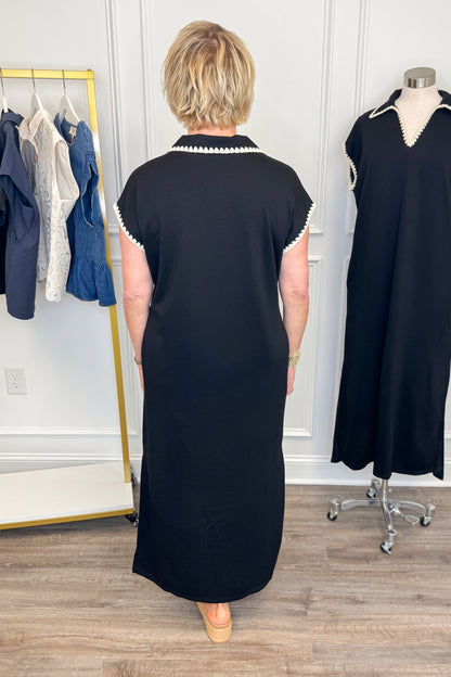 Back view of woman wearing Swagger Boutique’s Black Whipstitch Midi Dress by Entro with sandals with clothing hanging in the background.