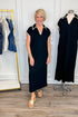 Front view of woman wearing Swagger Boutique’s Black Whipstitch Midi Dress by Entro with sandals with clothing hanging in the background.