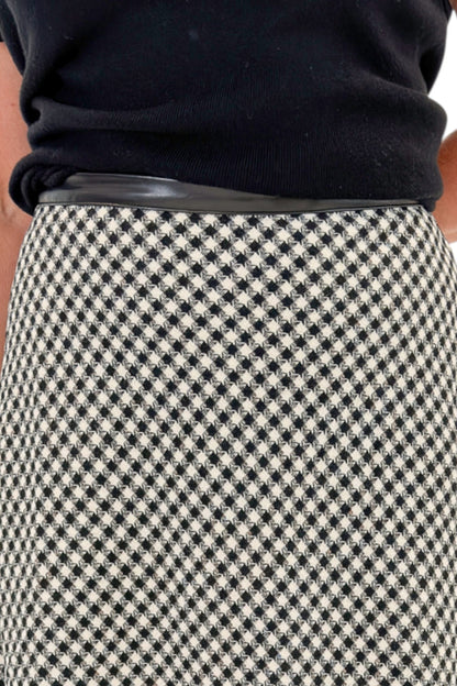 Front detail view of woman wearing Swagger Boutique’s Black Shirred Cap Sleeve Sweater with Black &amp; White Plaid Midi Skirt against white studio background.